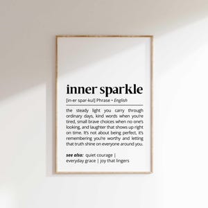 May include: A framed print featuring the phrase "inner sparkle" in a black, bold font. The definition of the phrase is below the title, in a smaller font. The frame is light brown, and the background is white.