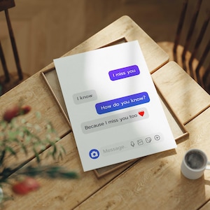 Könnte beinhalten: Eine weiße Karte mit einer simulierten Textnachrichten-Konversation. Die Nachrichten lauten: „Ich vermisse dich“, „Ich weiß“, „Woher weißt du das?“ und „Weil ich dich auch vermisse ❤️“. Die Karte liegt auf einem Holztisch mit einer kleinen Kaffeetasse.