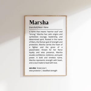 May include: A framed print featuring the name "Marsha" in a bold font. The text below provides a definition, explaining the name's meaning, Latin origins, and associated qualities like courage and leadership.