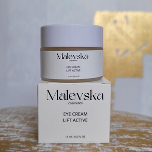 May include: A white jar of Malevska cosmetics eye cream with the text "Eye Cream Lift Active 15 ml / 0.5 FL OZ" on the label. The jar is sitting on top of a white box with the same text.