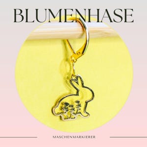 Könnte beinhalten: Goldfarbener Metall-Maschenmarkierer in Form eines Hasen mit Blumen in der Silhouette. Der Text "BLUMENHASE" befindet sich oben im Bild und "MASCHENMARKIERE" unten.
