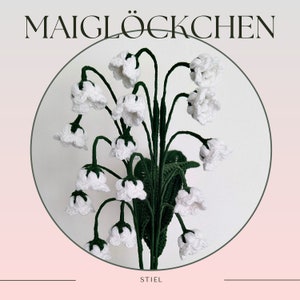 Può includere: Un bouquet di mughetti all'uncinetto bianco con steli e foglie verdi. I fiori sono disposti in cerchio e il testo "MAIGLÖCKCHEN" è nella parte superiore dell'immagine. Il testo "STIEL" è nella parte inferiore dell'immagine.