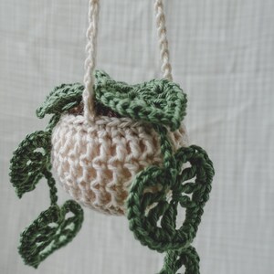 Peut inclure: Un porte-plante suspendu en crochet fait main. Le pot beige est orn&eacute; de feuilles vertes au crochet. Les cordons de suspension sont de couleur cr&egrave;me. Un objet d&eacute;coratif pour ajouter une touche de nature.