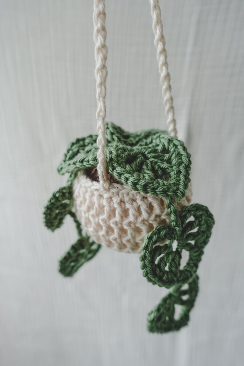 Peut inclure: Un cache-pot suspendu au crochet, de couleur cr&egrave;me et vert. Le panier cr&egrave;me est orn&eacute; de feuilles vertes et suspendu par une corde cr&egrave;me. Cet objet fait main est id&eacute;al pour les petites plantes et ajoute une touche de charme artisanal.