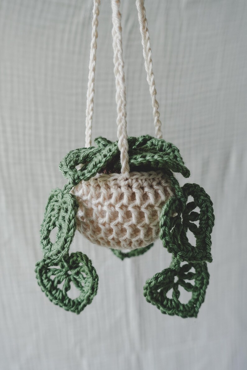 Peut inclure: Un porte-plante en crochet fait &agrave; la main. Le pot est de couleur cr&egrave;me avec un motif de feuilles vertes. Les feuilles sont vert fonc&eacute; et sont attach&eacute;es au pot cr&egrave;me. Le support est suspendu par trois cordons cr&egrave;me.