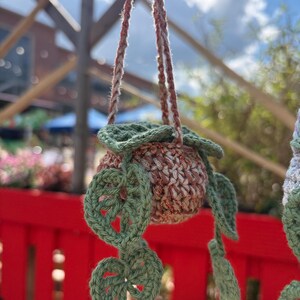 Peut inclure: Un pot de fleurs suspendu au crochet fait &agrave; la main. Le pot est un m&eacute;lange de fil marron et beige avec un bord vert et des feuilles vertes d&eacute;coratives. Les cordons de suspension sont marron et beige. Le pot est con&ccedil;u pour contenir une petite plante.