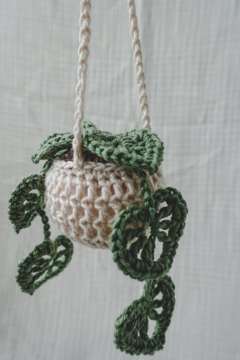 Peut inclure: Un porte-plante suspendu en crochet fait main. Le pot beige est orn&eacute; de feuilles vertes au crochet. Les cordons de suspension sont de couleur cr&egrave;me. Un objet d&eacute;coratif pour ajouter une touche de nature.