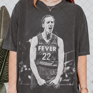 Könnte beinhalten: Dunkelgraues T-Shirt mit einem Schwarz-Weiß-Bild einer Basketballspielerin in einem Fever-Trikot mit der Nummer 22. Das Trikot hat auch das Salesforce-Logo. Die Spielerin schreit mit offenem Mund.