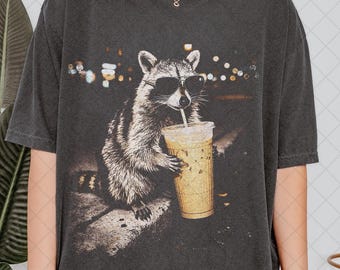 Camiseta unisex con mapache bebiendo café helado, divertida camiseta con meme de animales, ideal para amantes del café.