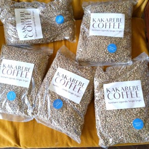 Op de afbeelding: Zes zakken groene koffiebonen met het label "Kakarebe Coffee" met de tekst "Northern Uganda Single Origin".
