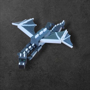 Könnte beinhalten: Ein schwarzes und weißes Plastikmodell des Enderdrachen aus dem Videospiel Minecraft. Der Drache hat große Flügel und einen langen Schwanz. Die Augen des Drachen leuchten grün.