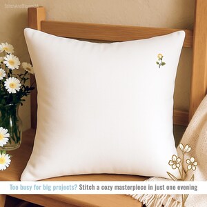 May include: A white square pillow with a small embroidered yellow flower. The pillow is on a wooden chair with a vase of white flowers. Text on the image reads: "Too busy for big projects? Stitch a cozy masterpiece in just one evening."