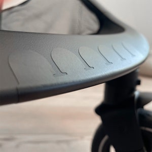 Puede incluir: Primer plano de un cochecito negro con una capota de malla y un parachoques de goma texturizado con protuberancias elevadas.