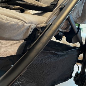 Puede incluir: Un cochecito negro con un asiento de tela gris y una cesta de almacenamiento de malla negra debajo.