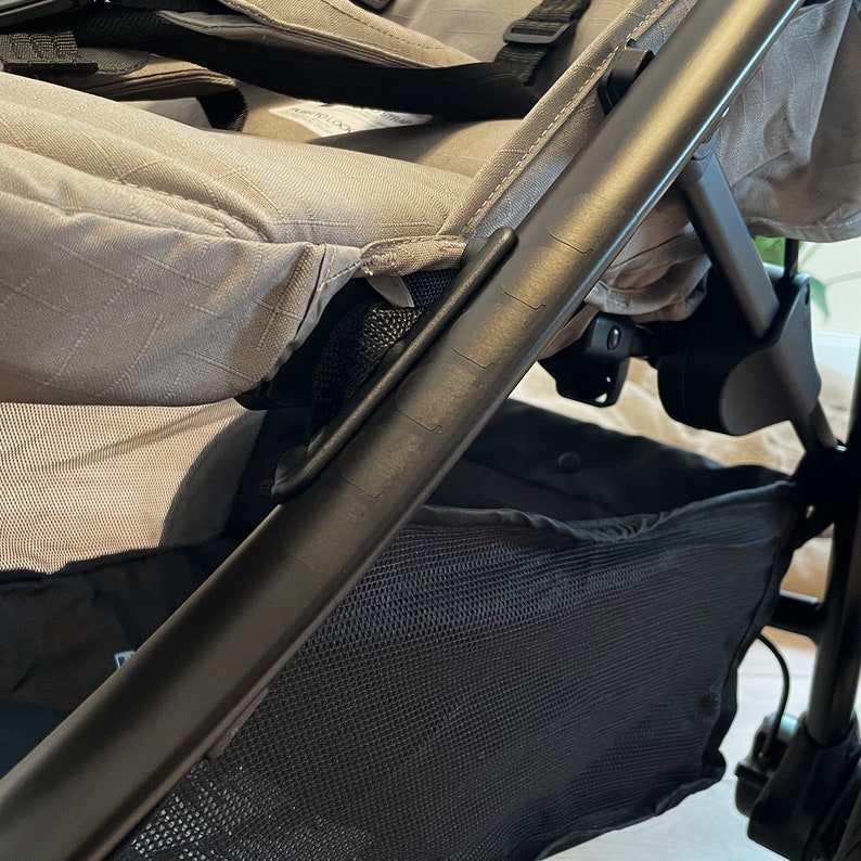 Puede incluir: Un cochecito negro con un asiento de tela gris y una cesta de almacenamiento de malla negra debajo.