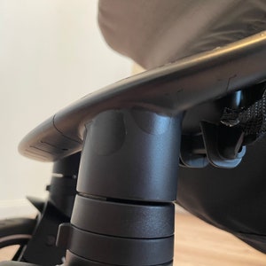 Puede incluir: Primer plano del marco de pl&aacute;stico negro de un cochecito, que muestra las ruedas giratorias y el manillar ajustable.