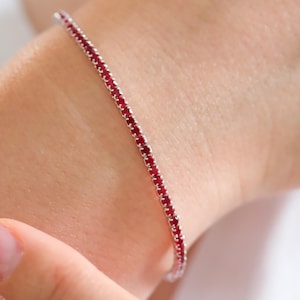 Peut inclure: Un bracelet argenté délicat avec une rangée de petites pierres précieuses rouge vif.