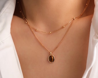 May include: A gold layered necklace with a brown oval pendant featuring a tiger's eye stone.