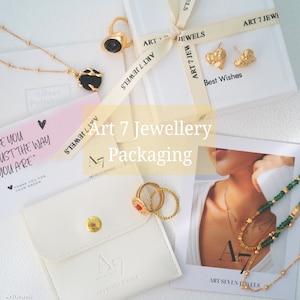 May include: A white box with the text "Art 7 Jewellery Packaging" on it. The box is open and there are several gold jewelry pieces inside, including rings, earrings, and a necklace. The jewelry is displayed on a white background.