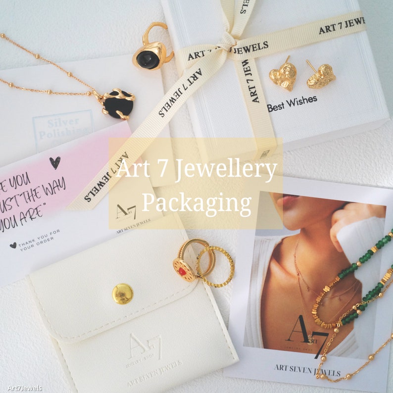 May include: A white box with the text "Art 7 Jewellery Packaging" on it. The box is open and there are several gold jewelry pieces inside, including rings, earrings, and a necklace. The jewelry is displayed on a white background.