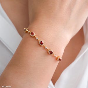 Peut inclure: Un bracelet en or orné de pierres précieuses rouges ovales et de petites pierres claires. Le bracelet est porté au poignet, mettant en valeur le design délicat. Il s'agit d'un bijou.