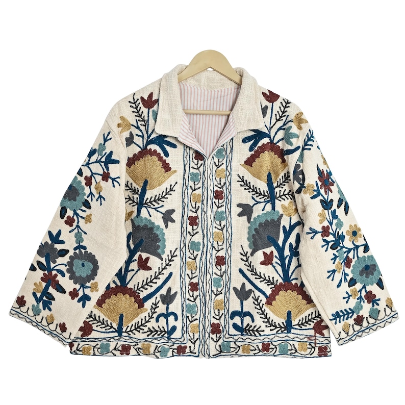 May include: Cream-colored jacket with intricate floral embroidery in shades of blue, gold, and burgundy. The jacket features a collared neckline and a striped lining. The embroidery is detailed and covers the front, sleeves, and back of the jacket.