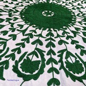 May include: White textile with a detailed green embroidered floral pattern. The design features a central circular motif with radiating leaf and floral elements. The embroidery is dense and creates a textured appearance.