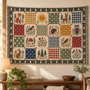 Könnte beinhalten: Eine gewebte Wandteppichdecke mit einem Raster aus zwanzig Quadraten, die Illustrationen von Fuchs, Sonne, Hirsch, Eule, Igel, Kaninchen, Vögeln, Pilzen, Blumen, Bäumen sowie verschiedene Muster wie Vichy-Karo, Streifen und Sterne zeigt.