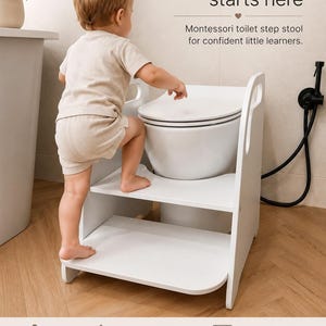 Puede incluir: Un taburete de madera blanca para inodoro con dos niveles y asas laterales. El texto en la imagen del producto dice: Independence starts here, Montessori toilet step stool for confident little learners, Encourages independence, Stable & safe design, Natural birch plywood, Fits most toilets, Made with care in Europe.