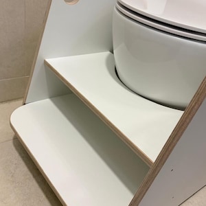 Pode incluir: Um banco de dois degraus branco com bordas de contraplacado, apresentando o texto WHITE MEL impresso no painel lateral superior. A estrutura inclui um recorte de al&ccedil;a no topo e um acabamento de superf&iacute;cie branco liso nos degraus.