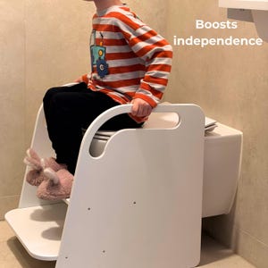 May include: A white toilet step stool with a handle, designed to help children reach the toilet. The stool has a step and a platform. The image includes the text "Boosts independence".
