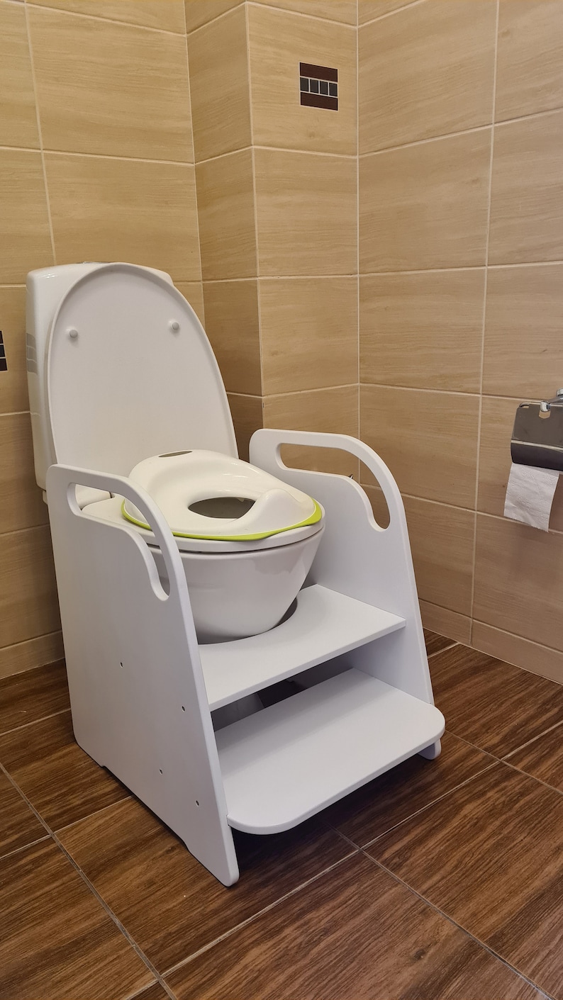 Pode incluir: Um degrau de aprendizagem em madeira branca com pegas laterais integradas e dois n&iacute;veis, concebido para encaixar &agrave; volta de uma sanita branca padr&atilde;o. Um assento de treino branco e verde-lima est&aacute; colocado sobre a tampa.