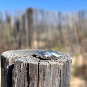 May include: A silver ring with a unique, abstract design. The ring is sitting on a weathered wooden post.