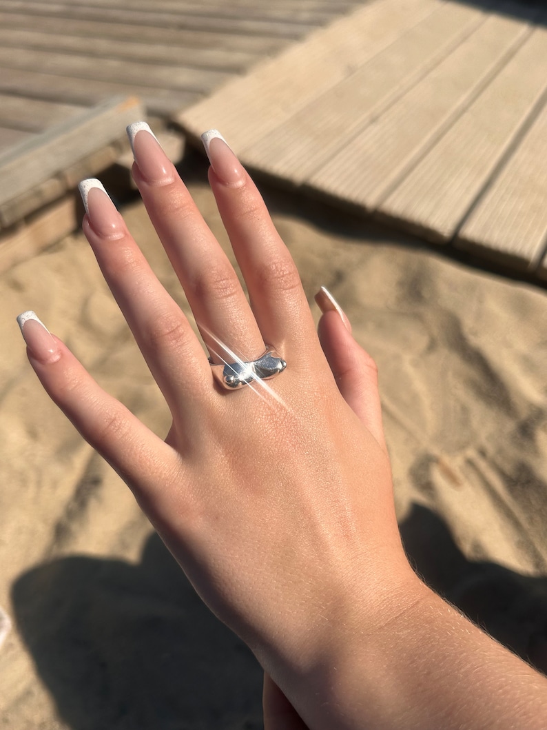 May include: A silver ring with a unique, abstract design. The ring is shaped like two rounded, connected forms.