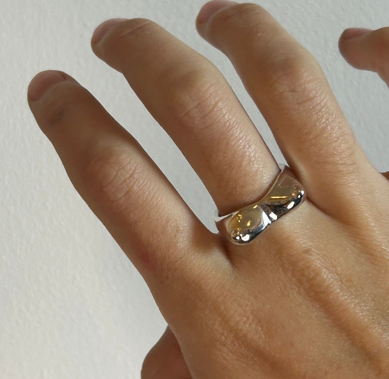 May include: A silver ring with an organic, asymmetrical design. The ring is worn on a person's finger.