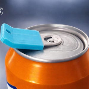 May include: A bright blue plastic soda can opener tool attached to the silver metal pull tab of an orange aluminum beverage can. The tool features a rectangular handle with a small circular hole at the end, designed to assist in lifting the tab.