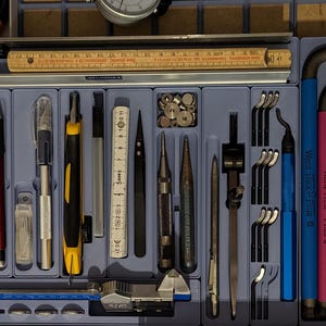 May include: A blue plastic tool organizer tray containing a variety of precision instruments including a wooden folding ruler, a metal caliper, tweezers, a compass, a set of Wera Hex-Plus L-keys, a utility knife, a pencil, and various small metal components.