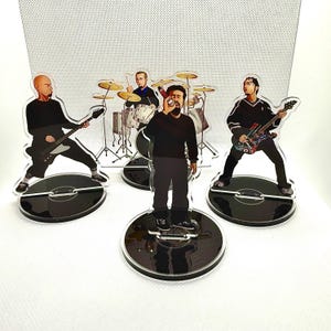 May include: Acrylic band figurines featuring a drummer, guitarist, and vocalist. The band members are depicted in black outfits, standing on black vinyl record bases. The background is a light gray.