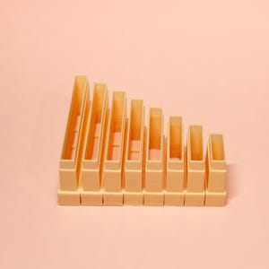 Peut inclure: Un organiseur de bureau pêche clair avec huit compartiments de hauteurs variables. L'organisateur est fait d'un matériau solide et mat et repose sur un fond pêche assorti. Les compartiments sont ouverts en haut et inclinés.