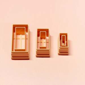 May include: Three sets of nested rectangular cookie cutters in a light peach colour. Each set consists of two rectangular frames of varying sizes, arranged in descending order from left to right, showing a clean, structured, and uniform design.