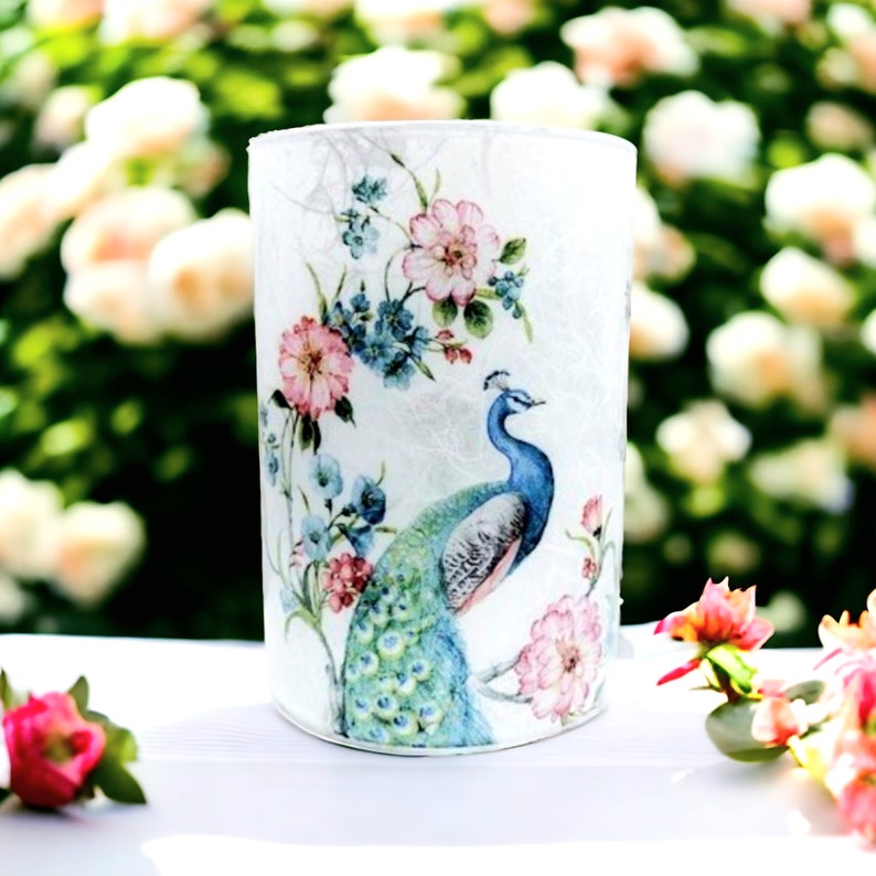 May include: A white cylinder candle holder with a floral and peacock design. The design features pink, blue, and green colors.