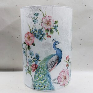May include: A white glass candle holder with a floral and peacock design. The design features pink, blue, and green colors.