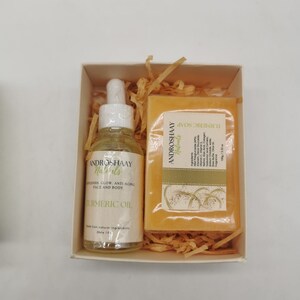 May include: A gift box set containing a small bottle of turmeric oil and a bar of turmeric soap. Both products are labeled "Androshaay Naturals" and feature a yellow and green color scheme. The oil bottle is 30 ml and the soap is 100 g.