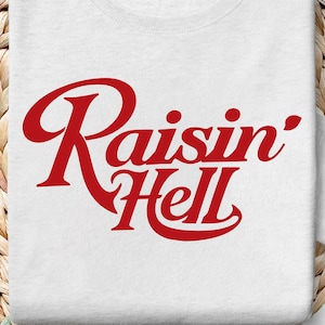 Puede incluir: Camiseta blanca con texto rojo que dice "Raisin' Hell" sobre un fondo de mimbre tejido.