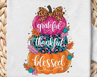 Może przedstawiać: Biała bluza z nadrukiem trzech ułożonych na sobie dyni z napisami "grateful", "thankful" i "blessed". Dynie są ozdobione wzorem lamparta, różowymi sercami i turkusowymi i złotymi akcentami.