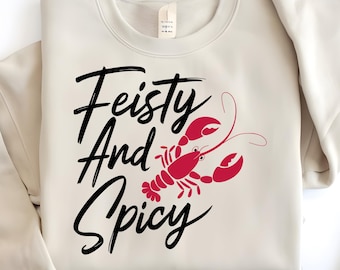 May include: A beige sweatshirt with the text "Feisty And Spicy" in black lettering and a red lobster illustration.