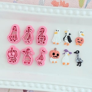 Könnte beinhalten: Eine Sammlung von Halloween-Ausstechern und Dekorationen. Die rosa Ausstecher sind in Form von Geistern, Enten und Kürbissen. Die Dekorationen umfassen Enten und Kürbisse in Halloween-Kostümen.