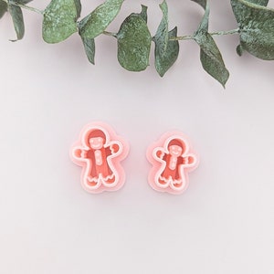 May include: Two pink gingerbread man cookie cutters, one larger than the other, on a light pink background.