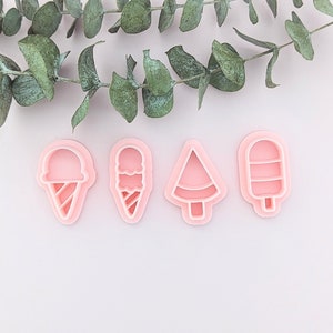 May include: Four pink plastic cookie cutters shaped like an ice cream cone, ice cream, a tree, and a popsicle. A sprig of green eucalyptus is at the top of the image. The cutters are on a white background.
