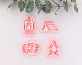 May include: Four pink plastic cookie cutters shaped like a lantern, a tent, a camper van, and a campfire.